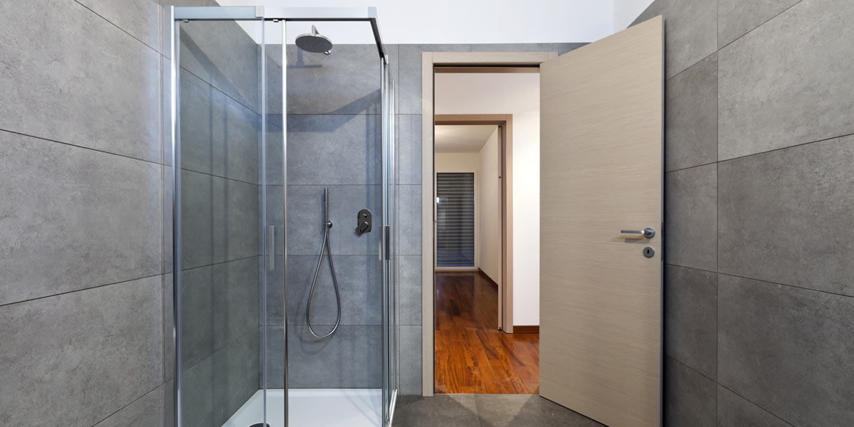 A modern shower with tile walls, glass doors and a fiberglass floor pan in room.