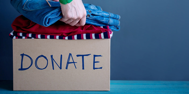 Person Placing Clothes Into a Cardboard Box That Says, “Donate”