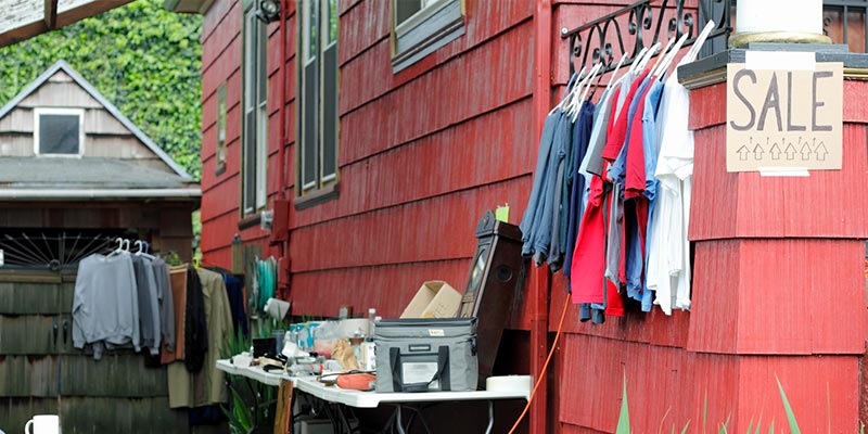 Clothes and Other Items Set Up on the Side of a Red House With a “Sale” Sign